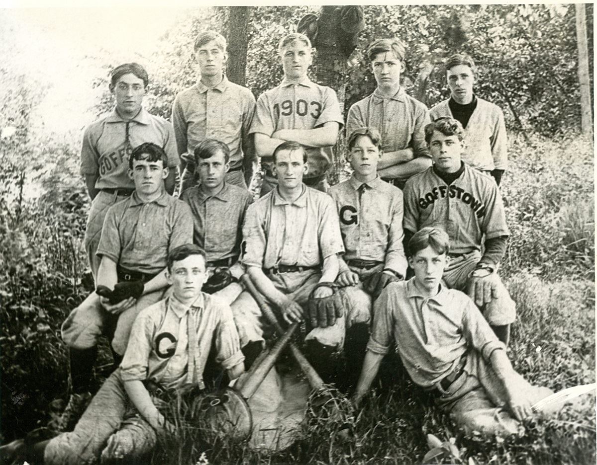 12 baseball players in Goffstown uniforms in 1903 sit and stand outdoors.