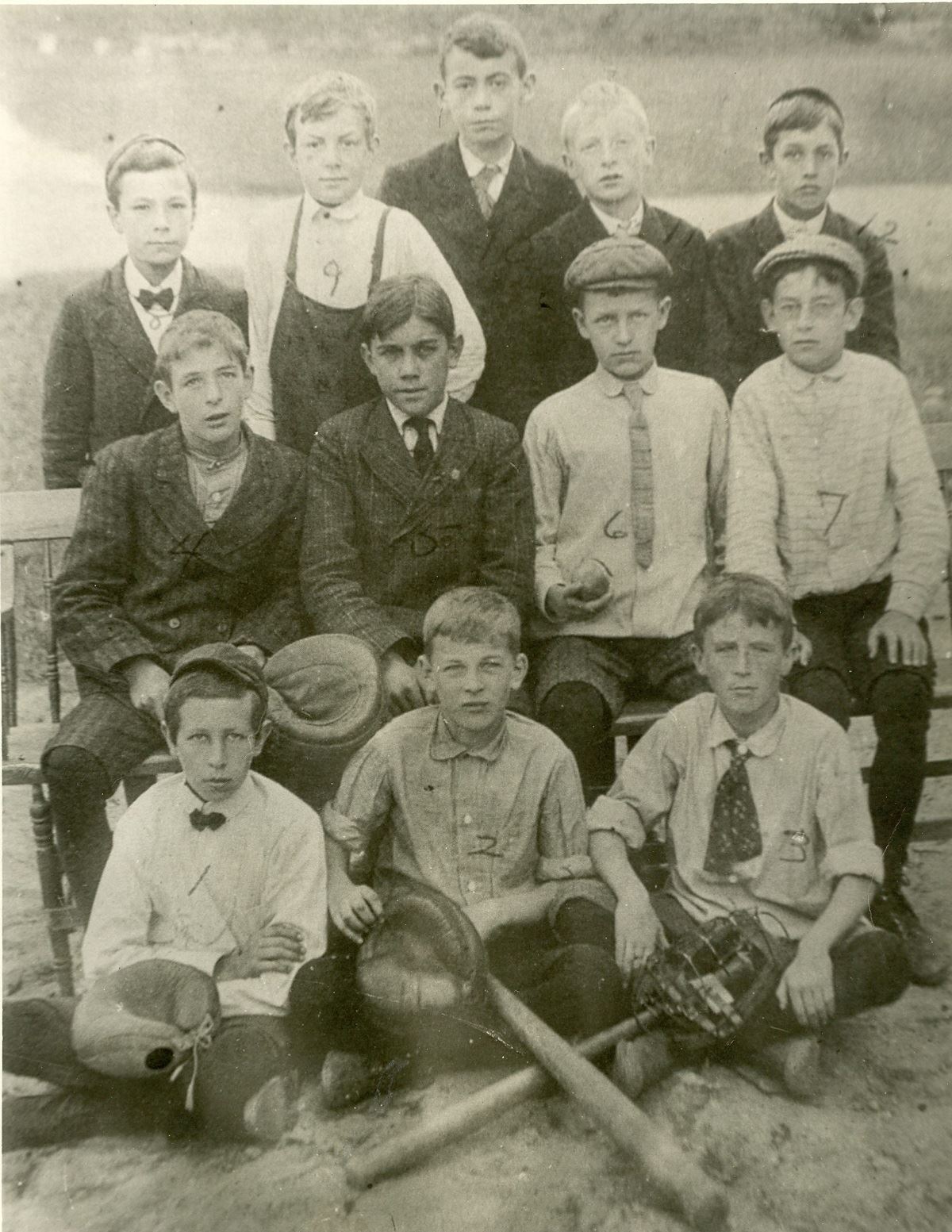 13 baseball players in early 1900s sit and stand outdoors in suits ties and caps.